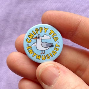 Könnte beinhalten: Ein blauer und gelber Knopf mit einer Cartoon-Möwe und dem Text "Chippy Tea Enthusiast."