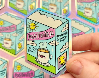 May include: A holographic sticker featuring a cartoon tea box design. The box is light blue with a pink banner that reads "POSITIVITEA." The design includes a smiling sun, clouds, and a teacup with heart-shaped steam. Text reads "You can brew it!" and "goodness in every cup."