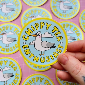 May include: Round sticker with a cartoon seagull illustration. The seagull is white and gray with an orange beak and feet, set against a light blue background. The sticker has yellow text that reads "CHIPPY TEA ENTHUSIAST".