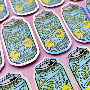 May include: A set of holographic stickers featuring a blue can with a yellow lemon and the text "Squeeze the Day! You got this! Motivational Lemonade".
