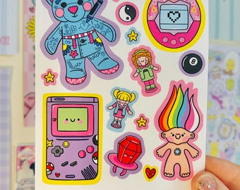 May include: A sticker sheet featuring 90s-themed illustrations including a blue bear with tattoos, a pink digital pet, a purple handheld game console, a rainbow-haired troll, a magic 8-ball, and small icons. Text at the bottom reads 90S NOSTALGIA WATERPROOF STICKERS KELLYLOU.CO.UK.