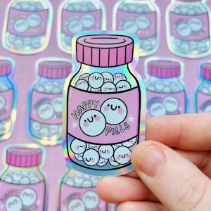 May include: A holographic sticker depicting a pink jar labelled "Happy Pills." The jar is filled with smiling, round pills. The sticker has a pink lid and a holographic, iridescent effect.