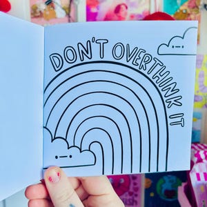 May include: A blue notebook with a rainbow and the text "Don't overthink it" in black. The notebook has a cloud with a face at the top.