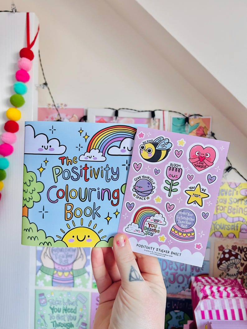 May include: A pink and blue sticker sheet with a variety of positive messages and illustrations. The sheet includes a rainbow, a bee, a flower, a star, a cake, and a heart. The text on the sheet includes "You Deserve Joy", "Give Yourself Space", "Bloom", "Make Your Future Better Than Your Past", and "Love Yourself".