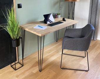 May include: A light wood desk with black hairpin legs and a gray fabric chair. The desk has a laptop, keyboard, and mouse on it. There is a black plant stand with a green plant in it. There are two framed pictures on the wall behind the desk.