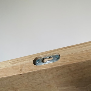May include: Close-up of a wooden shelf with a metal hanging bracket attached to the underside. The bracket is secured with two screws.