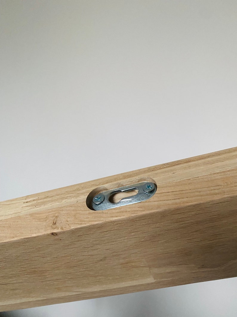 May include: Close-up of a wooden shelf with a metal hanging bracket attached to the underside. The bracket is secured with two screws.