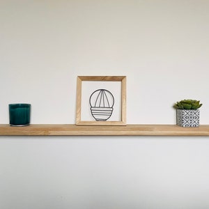 May include: A wooden shelf with a teal candle, a framed wire sculpture of a plant, and a small potted succulent plant.