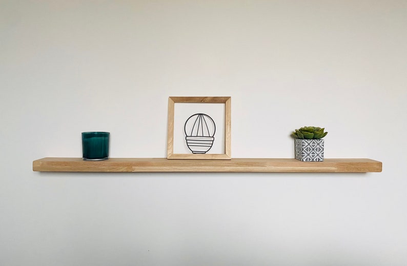 May include: A wooden shelf with a teal candle, a framed wire sculpture of a plant, and a small potted succulent plant.