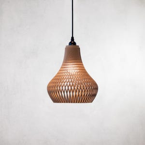 Może przedstawiać: Brązowa lampa wisząca z tkanym kloszem. Klosz ma pękaty kształt i wzór kraty, zawieszony na czarnym kablu. Światło jest włączone, oświetlając wnętrze klosza.