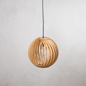 May include: A wooden pendant light with a round, slatted shade. The shade is made of light brown wood and has a black cord.