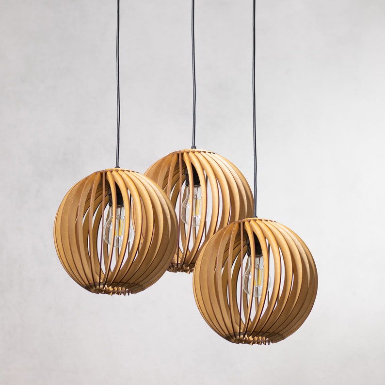 May include: Three wooden globe pendant lights hang from black cords against a white background. The lights are made of thin, light brown wood slats that create a geometric pattern. Each light has a clear light bulb inside.