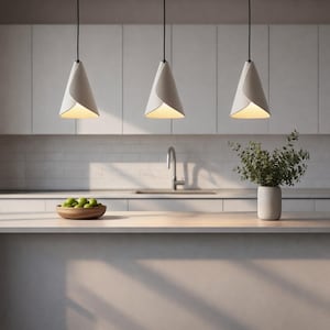 Three sculptural white pendant lights suspended above a modern kitchen island with white cabinetry and soft natural light.