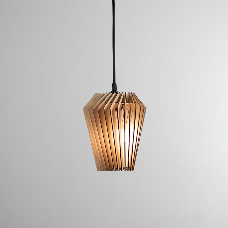 Pu&ograve; includere: Una lampada a sospensione in legno con un design geometrico. La luce &egrave; realizzata con sottili lamelle di legno marrone chiaro disposte a forma di ventaglio. La luce &egrave; appesa a un cavo nero.