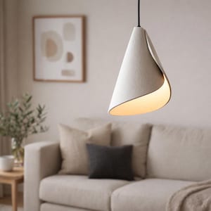 Handcrafted white pendant light with a sculptural folded form, hanging above a modern living room sofa and emitting a warm ambient glow.