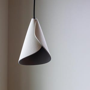 Modern 3D-printed pendant lamp with a folded sculptural shape, photographed unlit against a soft neutral background.