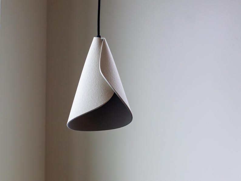 Modern 3D-printed pendant lamp with a folded sculptural shape, photographed unlit against a soft neutral background.