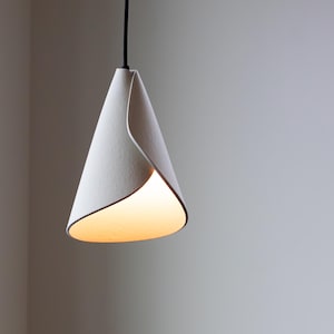 Handcrafted white 3D-printed pendant light with a twisted cone form, glowing warmly against a minimalist gray wall.