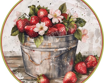May include: A circular sign featuring a watercolor illustration of a galvanized metal bucket overflowing with bright red strawberries and white blossoms. Additional strawberries are scattered on a wooden surface in the foreground.