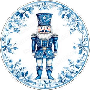 May include: A circular sign featuring a nutcracker illustration in shades of blue and white. The nutcracker wears a tall hat and uniform with floral patterns. A blue and white floral wreath border surrounds the central figure on a white background.