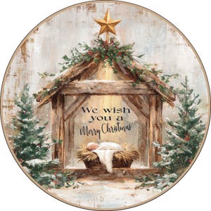 May include: A round Christmas-themed image featuring a nativity scene. A wooden stable is topped with greenery and a gold star. The text "We wish you a Merry Christmas" is displayed. Snow and evergreen trees frame the scene.