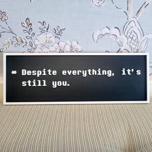 May include: A black framed sign with white letters that reads "* Despite everything, it's still you."
