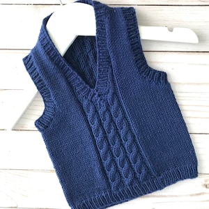 Puede incluir: Un chaleco de punto azul marino con un patrón de trenza y cuello en V.