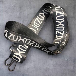 May include: Black and gray strap with white text reading "ZUXOZDR". The strap has silver-colored metal clasps and a buckle. The strap is made of a woven material.
