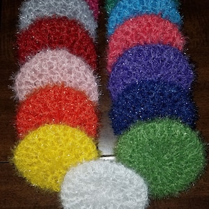 May include: A set of 12 colorful crocheted dishcloths, each with a different color and a fluffy texture. The dishcloths are arranged in a stack, with the white dishcloth at the bottom.