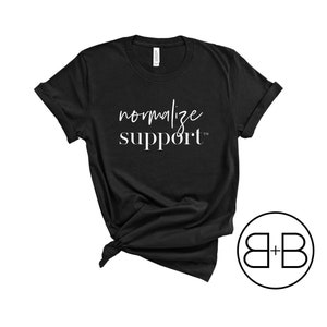 May include: Black t-shirt with white text that reads "normalize support" and a small trademark symbol. The shirt is knotted at the bottom and a black and white logo of "B+B" is in the bottom right corner.