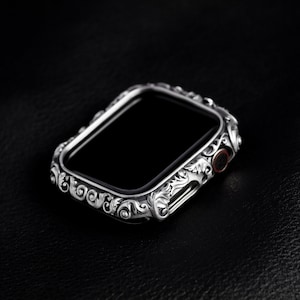 May include: A silver Apple Watch case with an ornate, detailed design. The case is made of metal and has a black screen.