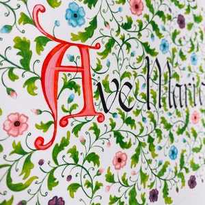 May include: A hand-painted floral design with the word "Ave Maria" written in black ink. The design features a variety of flowers in shades of pink, blue, and purple, as well as green leaves and vines.