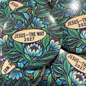 Puede incluir: Una colección de chapas redondas con un estampado floral en azul oscuro y verde con detalles en azul claro. Cada chapa tiene un óvalo central de color crema con el texto negro JESUS-THE WAY 2027 y varios nombres de ciudades.