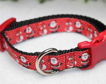 May include: Red and black dog collar with a festive Christmas pattern featuring Santa Claus and snowmen. The collar has a red plastic buckle and a silver metal D-ring.