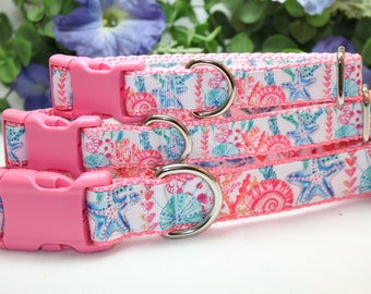 May include: Three pink dog collars with white fabric featuring a seashell and starfish pattern. The collars have silver metal D-rings and pink plastic buckles.