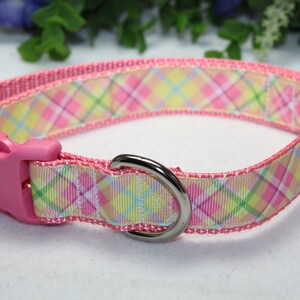 May include: Pink dog collar with a plaid pattern in shades of pink, yellow, and green. The collar has a pink plastic buckle and a silver metal D-ring.