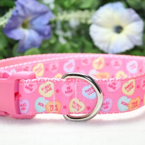 Puede incluir: Collar de perro rosa con una hebilla plateada y un anillo en D plateado. El collar est&aacute; decorado con un patr&oacute;n de corazones de caramelo rosa, azul y amarillo con varios mensajes, que incluyen "Sweet Love", "Be Mine" y "Hug Me".