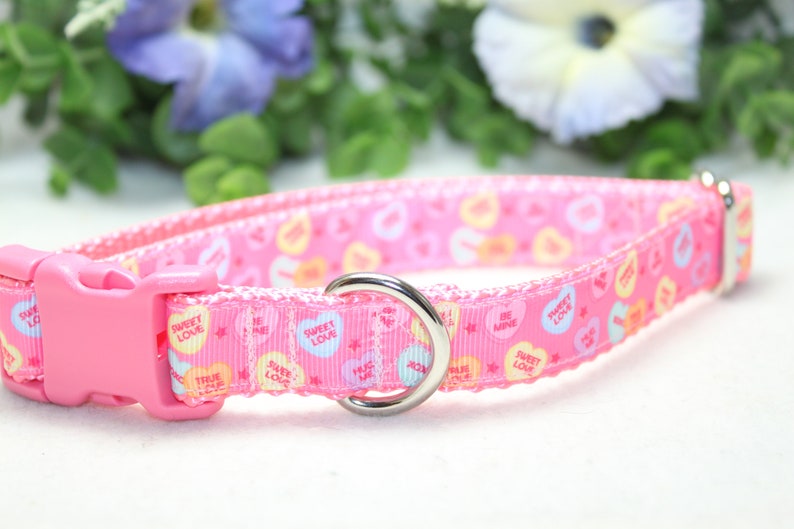 Puede incluir: Collar de perro rosa con un patr&oacute;n de corazones de caramelo de amor dulce. El collar tiene un anillo en D de metal plateado y una hebilla de pl&aacute;stico rosa.