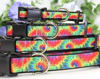May include: Four colorful tie-dye dog collars with black webbing and silver D-rings. The collars are stacked on top of each other, with the smallest collar on top and the largest collar on the bottom.