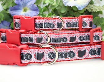 May include: Three red dog collars with a white and grey patterned design featuring the word "Ohio" and a black outline of the state of Ohio. The collars have red plastic buckles and silver D-rings.