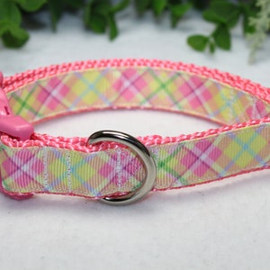 May include: Pink dog collar with a plaid pattern in shades of pink, yellow, and green. The collar has a plastic buckle and a metal D-ring.