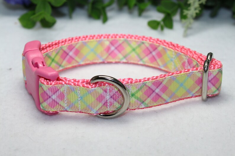 May include: Pink dog collar with a plaid pattern in shades of pink, yellow, and green. The collar has a plastic buckle and a metal D-ring.