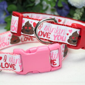 May include: Two dog collars with white background and pink and red accents. The collars feature a brown poop emoji with glitter and hearts. The text on the collars reads "I stinking love you".