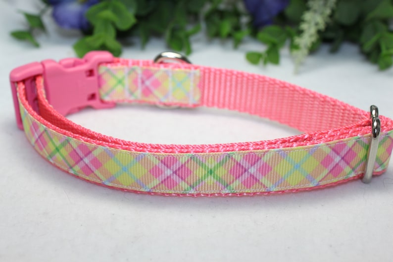 May include: Pink dog collar with a plaid pattern in pink, yellow, and green. The collar has a plastic buckle and a metal D-ring.