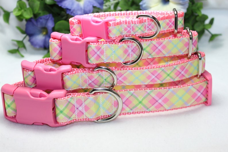 May include: Three pink dog collars with plaid patterns in yellow, green, and pink. The collars have pink plastic buckles and silver D-rings.