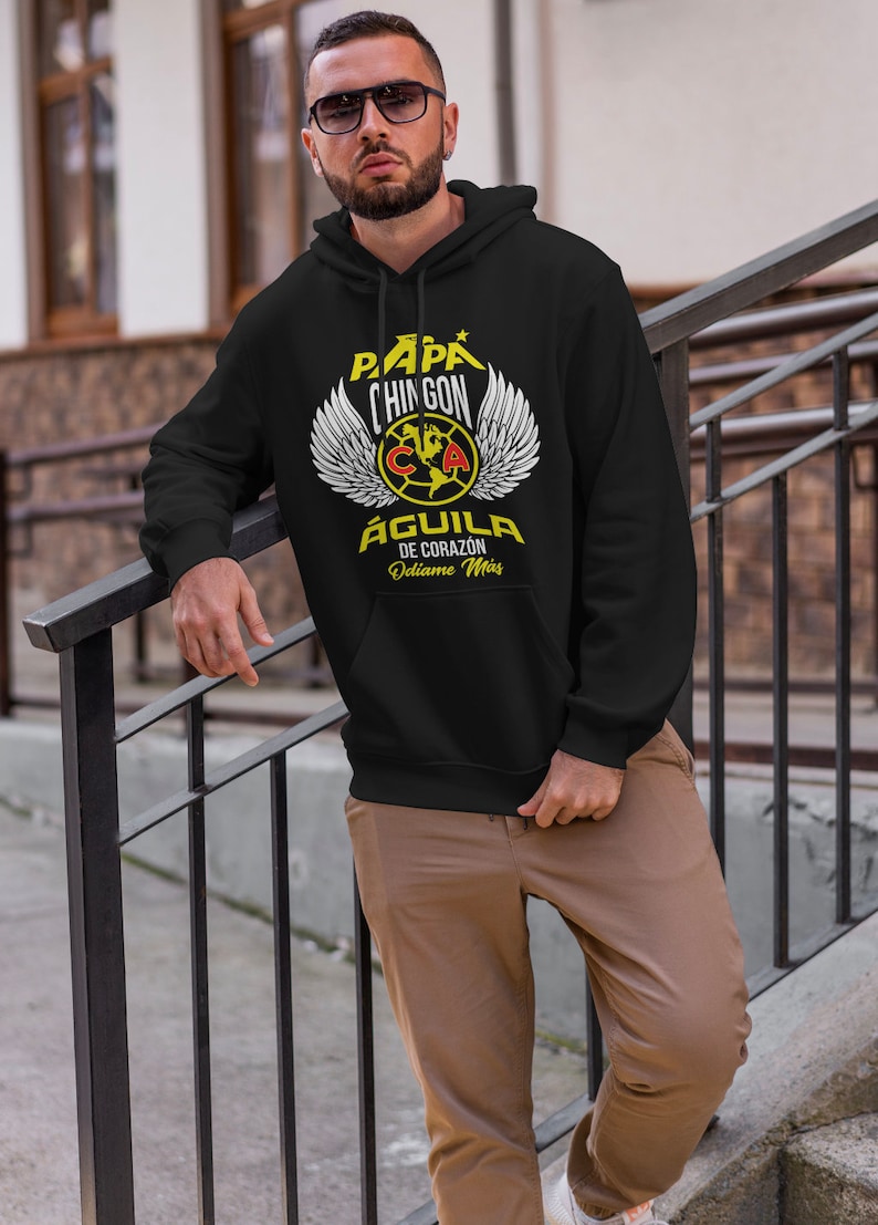 May include: Black hooded sweatshirt with a yellow and red graphic print of a winged eagle with the text "Pap&aacute; Chingon Aguila de Corazon Od&iacute;ame M&aacute;s".