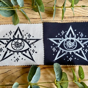 May include: Two fabric squares featuring a black and white print of an eye within a star. The star is encircled by smaller diamonds. One square is white with black print, the other is black with white print.