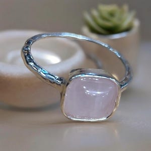 May include: A silver ring featuring a square-shaped, pale pink rose quartz gemstone.