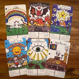 Pode incluir: Um conjunto de cartas de tarot desenhadas à mão com ilustrações coloridas. As cartas apresentam imagens de um arco-íris, um diabo, uma estrela, um sol, um olho e pentáculos. Cada carta tem texto e números manuscritos.