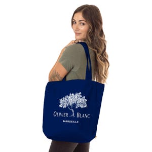 Peut inclure: Un sac fourre-tout bleu marine avec un motif d'arbre blanc et le texte "OLIVIER BLANC MARSEILLE". Le sac est porté sur l'épaule et présente un design simple. Le sac est fait d'un matériau durable.